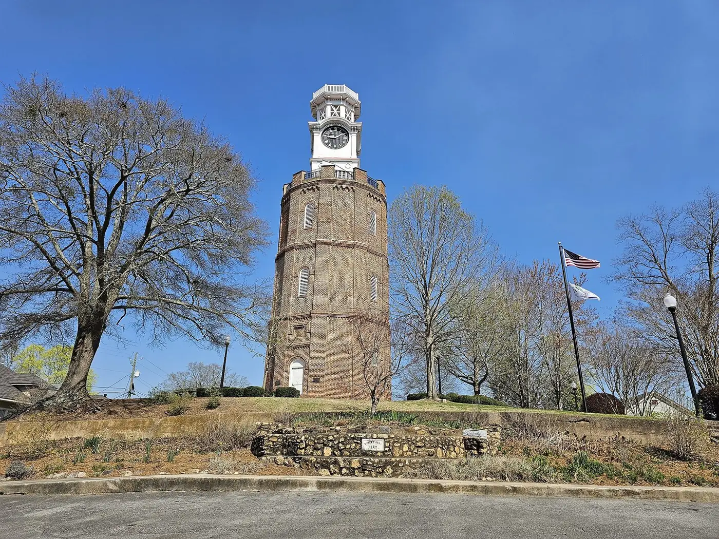 The brick Clock Tower on Neely Hill in Rome, Georgia, under a blue sky with bare trees around it