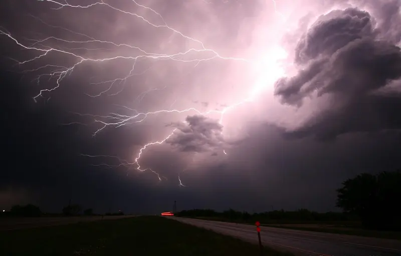 Lightning bolts across a dark purple sky over a road
